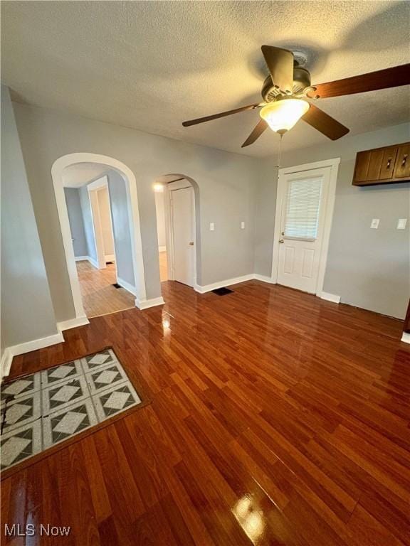 unfurnished living room with a textured ceiling, wood finished floors, arched walkways, baseboards, and ceiling fan