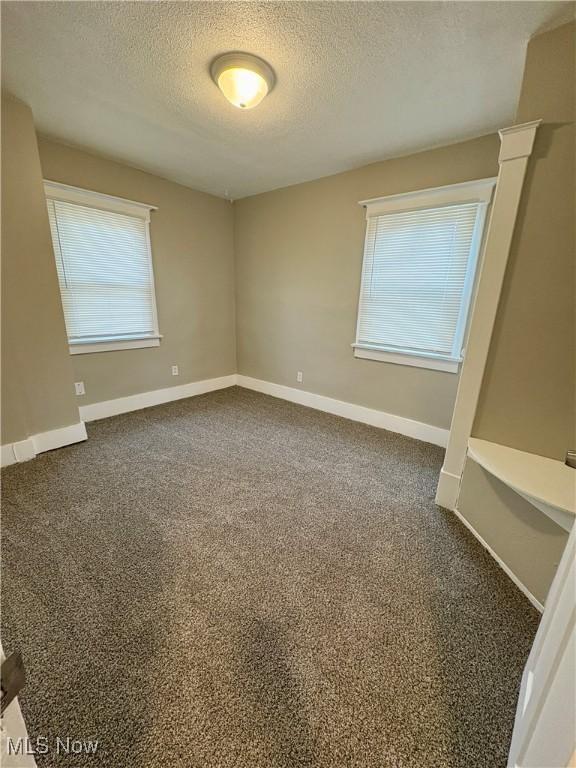 empty room featuring dark carpet, a textured ceiling, and baseboards