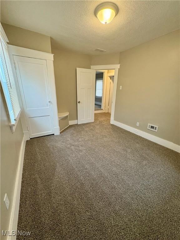 unfurnished bedroom with baseboards, visible vents, dark colored carpet, and a textured ceiling