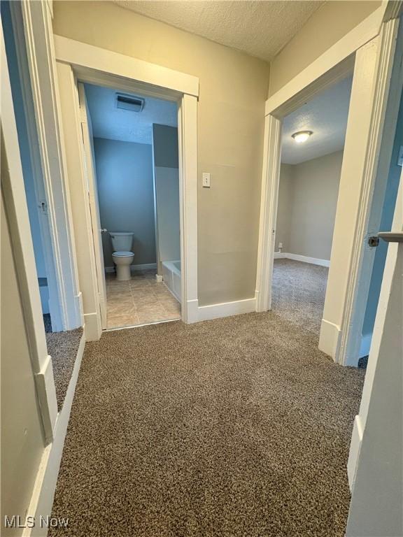 corridor featuring visible vents, baseboards, a textured ceiling, and carpet flooring