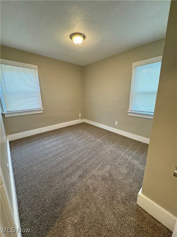 carpeted empty room with a textured ceiling and baseboards