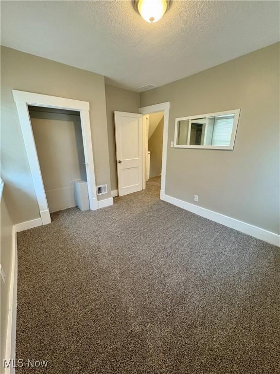 unfurnished bedroom with baseboards, carpet, visible vents, and a textured ceiling