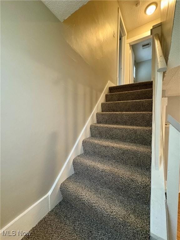 staircase with visible vents, carpet flooring, a textured ceiling, and baseboards