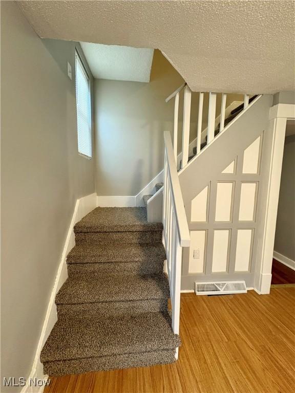 staircase with a textured ceiling, wood finished floors, visible vents, and baseboards