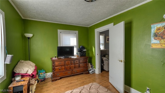 bedroom with baseboards, a textured ceiling, wood finished floors, and crown molding