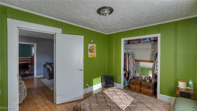 bedroom with a textured ceiling, wood finished floors, a closet, and ornamental molding