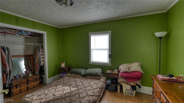 bedroom featuring ornamental molding, a textured ceiling, baseboards, and wood finished floors