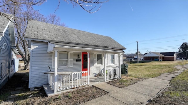 bungalow-style home with roof with shingles, covered porch, and a front lawn