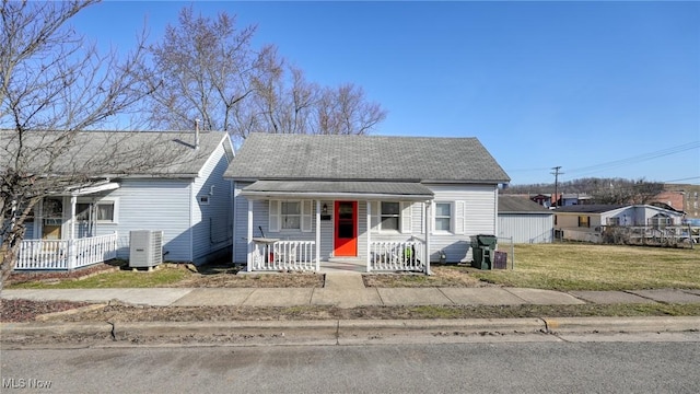 view of front of home with central AC unit, roof with shingles, covered porch, and a front lawn