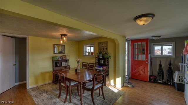 dining area with a wealth of natural light, arched walkways, baseboards, and wood finished floors