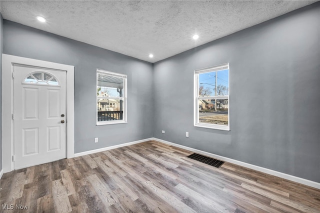 foyer entrance with visible vents, a textured ceiling, wood finished floors, recessed lighting, and baseboards