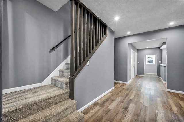 stairway with recessed lighting, a textured ceiling, baseboards, and wood finished floors