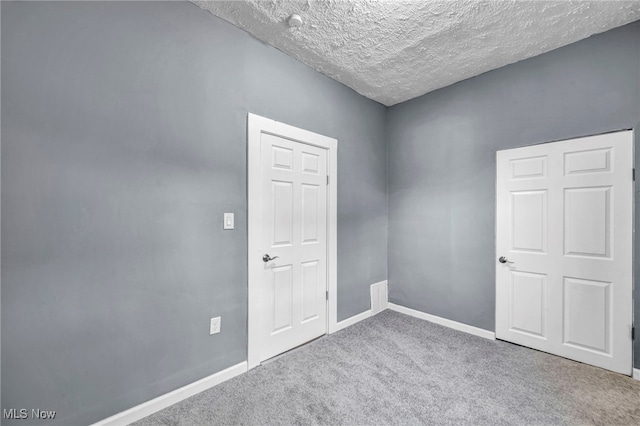 carpeted spare room featuring a textured ceiling and baseboards