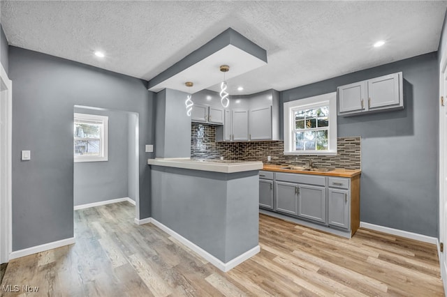 kitchen featuring backsplash, light wood-type flooring, wooden counters, and gray cabinetry