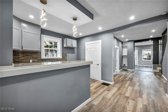 kitchen with baseboards, a peninsula, light wood-style flooring, decorative backsplash, and hanging light fixtures