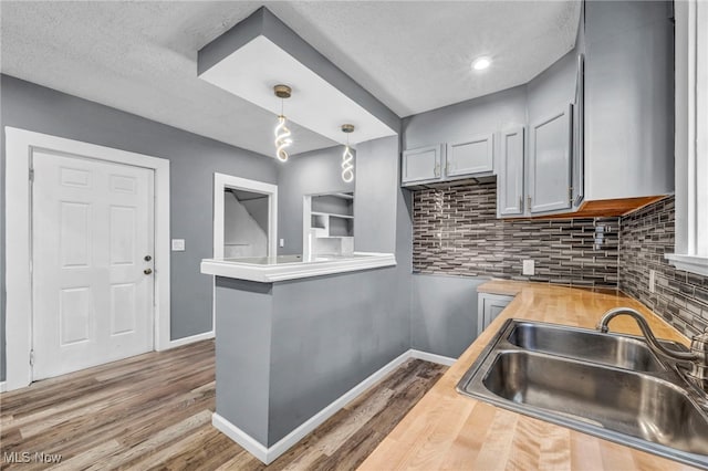 kitchen with a sink, decorative backsplash, baseboards, and wood finished floors