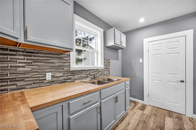 kitchen with tasteful backsplash, gray cabinets, light wood-style floors, wood counters, and a sink