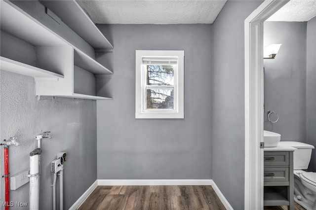 clothes washing area with baseboards, dark wood-type flooring, and a textured ceiling