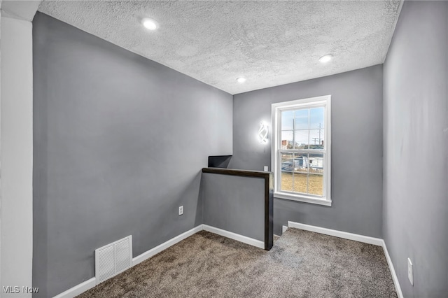 carpeted spare room with visible vents, a textured ceiling, and baseboards