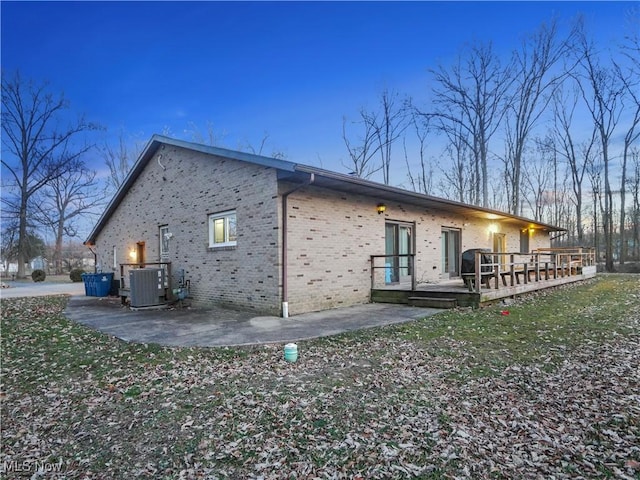 back of property with a wooden deck, brick siding, central AC unit, and a patio area