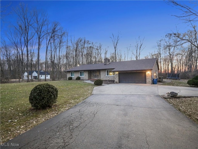 view of front of house with an attached garage, a front lawn, aphalt driveway, a trampoline, and brick siding