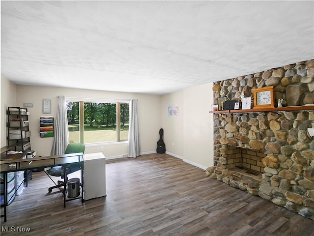 home office featuring baseboards, a stone fireplace, and wood finished floors