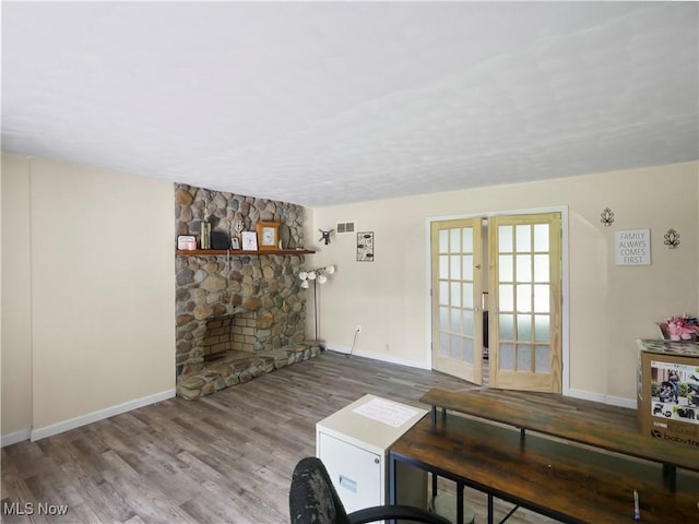 living area with visible vents, wood finished floors, french doors, a stone fireplace, and baseboards