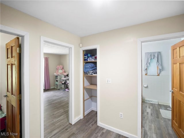 hall with visible vents, baseboards, and wood finished floors