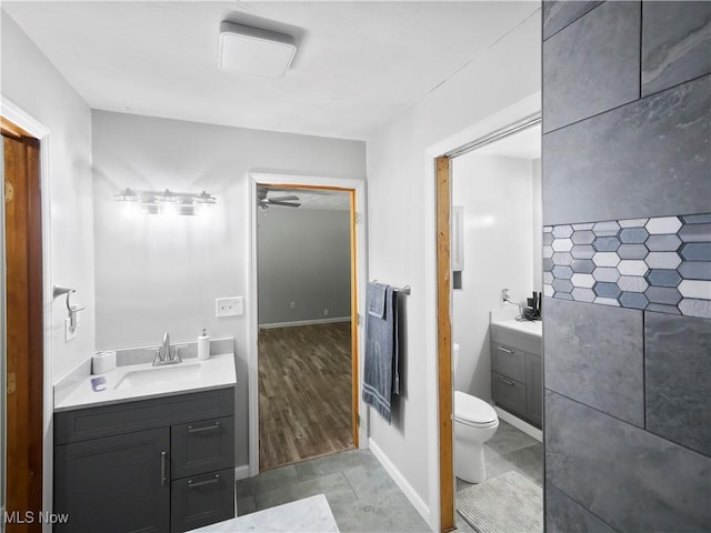 bathroom featuring a sink, toilet, baseboards, and two vanities