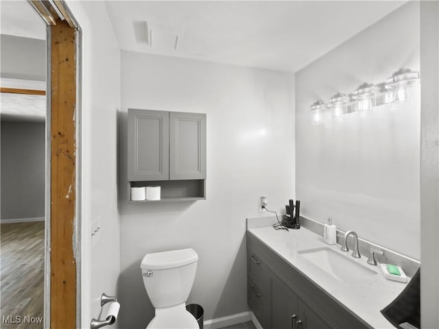 bathroom with vanity, toilet, wood finished floors, and baseboards