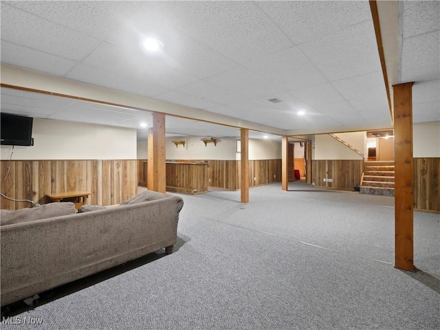 finished below grade area featuring wooden walls, carpet, a wainscoted wall, stairs, and a paneled ceiling