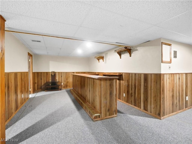 bar featuring wainscoting, a bar, wood walls, and carpet floors