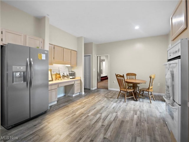 kitchen featuring light wood-style flooring, light brown cabinets, stainless steel fridge, baseboards, and built in study area