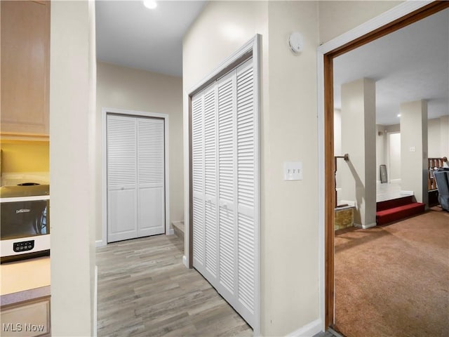 hallway featuring light colored carpet, light wood-type flooring, and baseboards