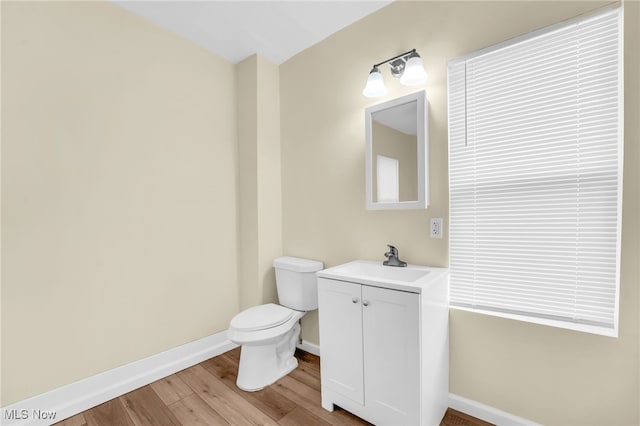 half bath featuring baseboards, toilet, wood finished floors, and vanity