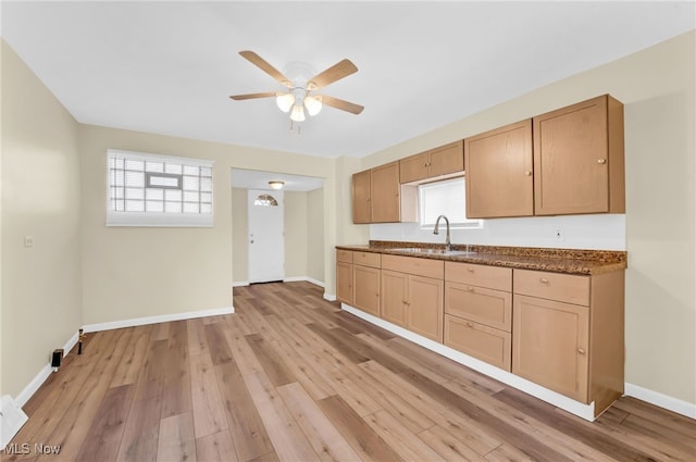 kitchen with light wood finished floors, ceiling fan, baseboards, dark stone countertops, and a sink