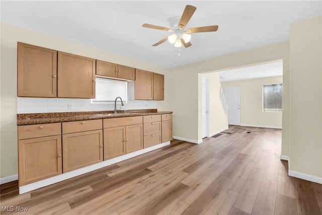 kitchen with dark stone countertops, a ceiling fan, baseboards, light wood finished floors, and a sink