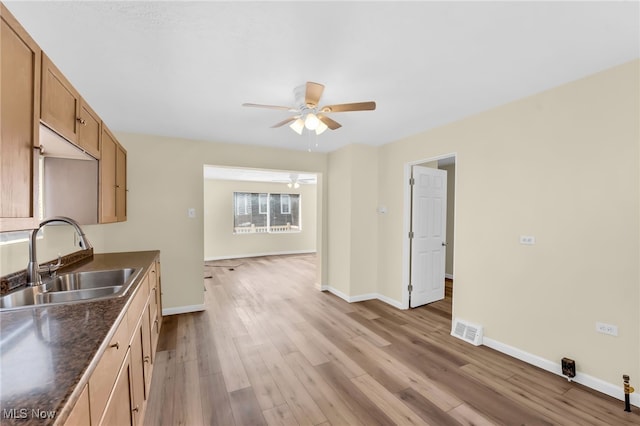 kitchen featuring dark countertops, visible vents, baseboards, light wood-style flooring, and a sink