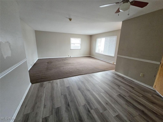 empty room with a baseboard radiator, baseboards, a ceiling fan, and wood finished floors