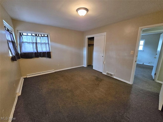 unfurnished bedroom with visible vents, a baseboard heating unit, baseboards, dark carpet, and a closet