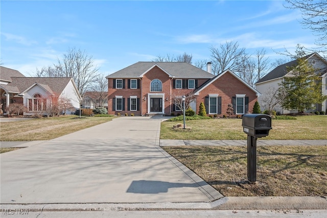 view of front of house with a front yard, brick siding, and driveway