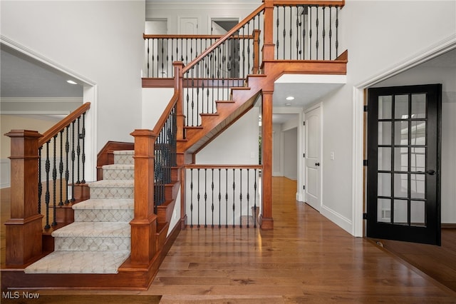 stairs featuring ornamental molding, a towering ceiling, and wood finished floors