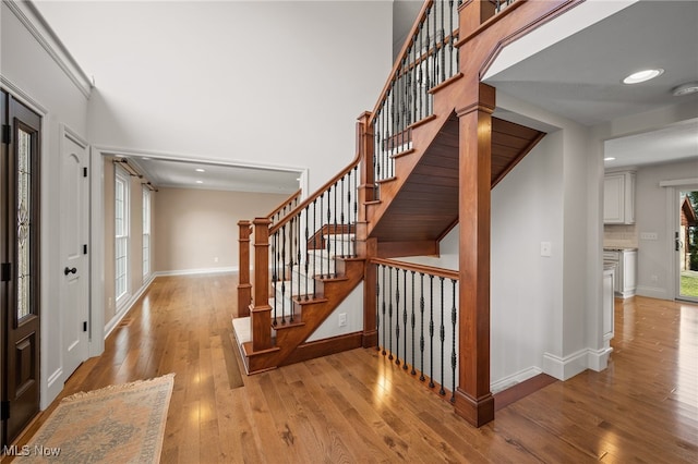 staircase featuring recessed lighting, baseboards, wood-type flooring, and a high ceiling