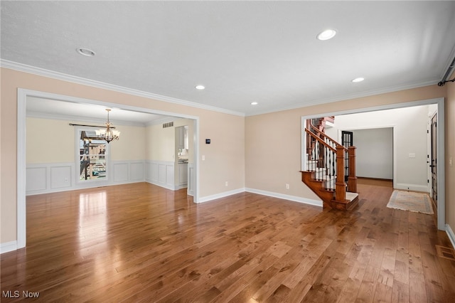 unfurnished living room with crown molding, stairs, an inviting chandelier, light wood-style floors, and a decorative wall