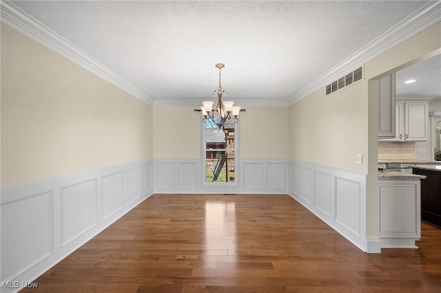 unfurnished dining area with wood finished floors, visible vents, crown molding, a decorative wall, and a chandelier