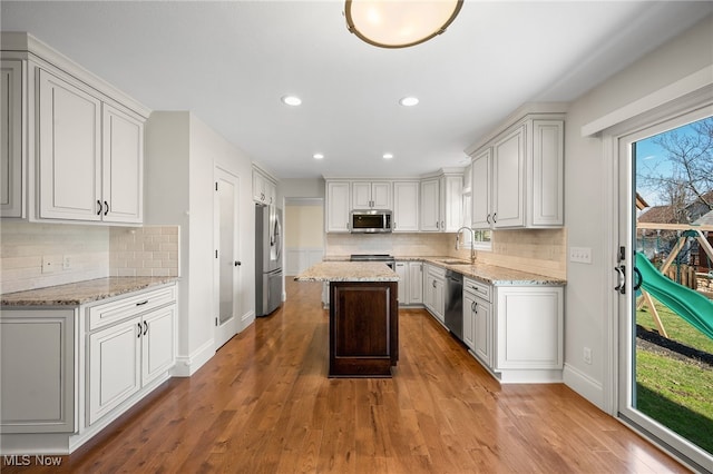 kitchen featuring a kitchen island, light stone counters, wood finished floors, stainless steel appliances, and a sink