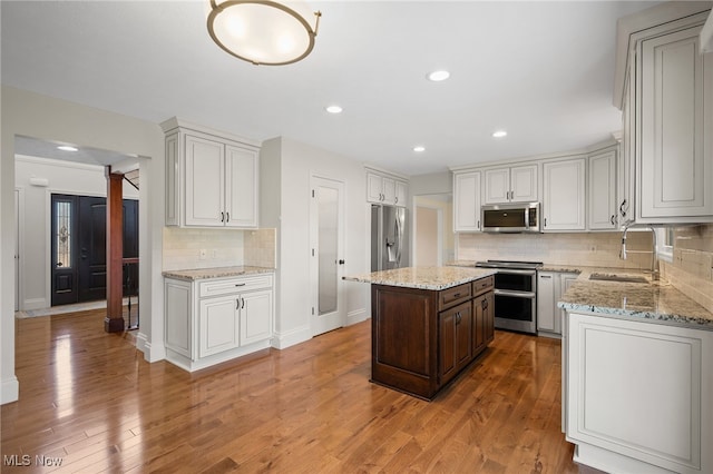 kitchen with light stone counters, appliances with stainless steel finishes, light wood-style floors, ornate columns, and a sink