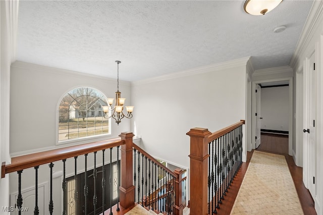 corridor with an upstairs landing, ornamental molding, an inviting chandelier, and wood finished floors