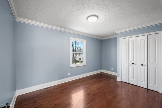 unfurnished bedroom with visible vents, dark wood-type flooring, baseboards, ornamental molding, and a closet