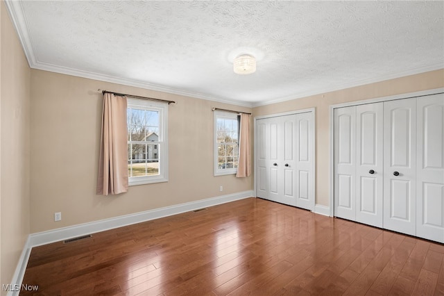 unfurnished bedroom featuring visible vents, wood-type flooring, baseboards, and multiple closets